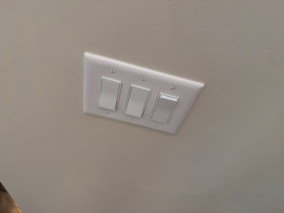 Existing white three-gang switch plate on a wall, photographed before dimmers were installed